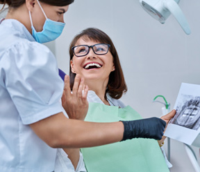 Woman smiling with dentist while reviewing X-ray