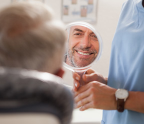 Man smiling at reflection in handheld mirror