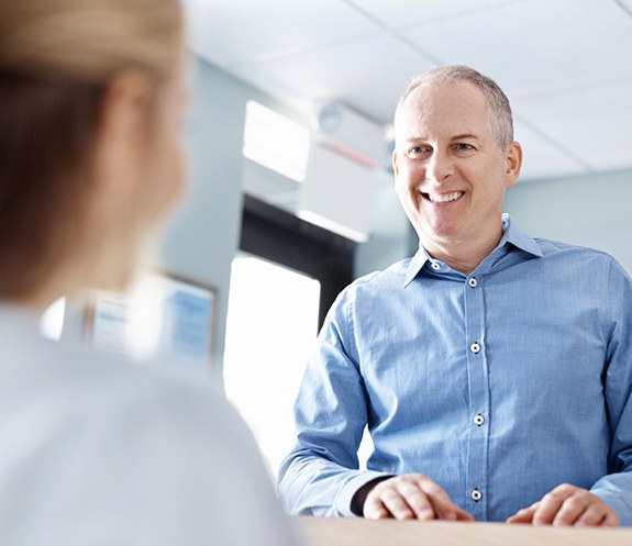 Dental patient smiling at team member behind reception desk